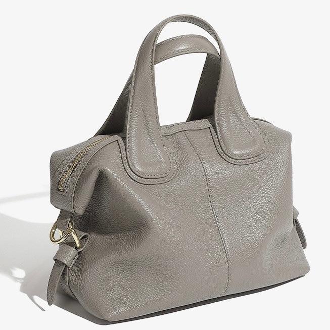 Taupe leather handbag with double handles, gold hardware, and zipper closure on white background