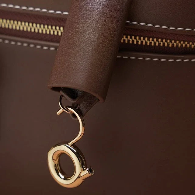 Brown leather bag with gold clasp, visible zipper and detailed stitching