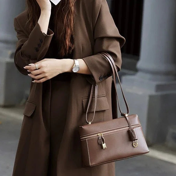 Woman in brown coat holding a brown leather handbag with gold hardware outdoors