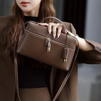 Woman in brown suit holding a brown leather crossbody handbag with gold hardware