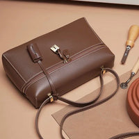 Brown leather handbag with gold hardware on tan background, leathercraft tools beside it
