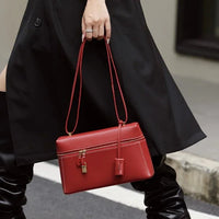 Woman in black trench coat holding stylish red leather handbag with lock on city street