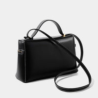 Black leather handbag with top handle and long shoulder strap on white background
