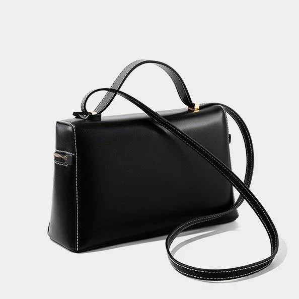 Black leather handbag with top handle and long shoulder strap on white background