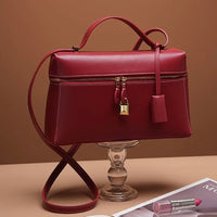 Elegant red leather handbag with gold lock on glass stand, pink lipstick nearby