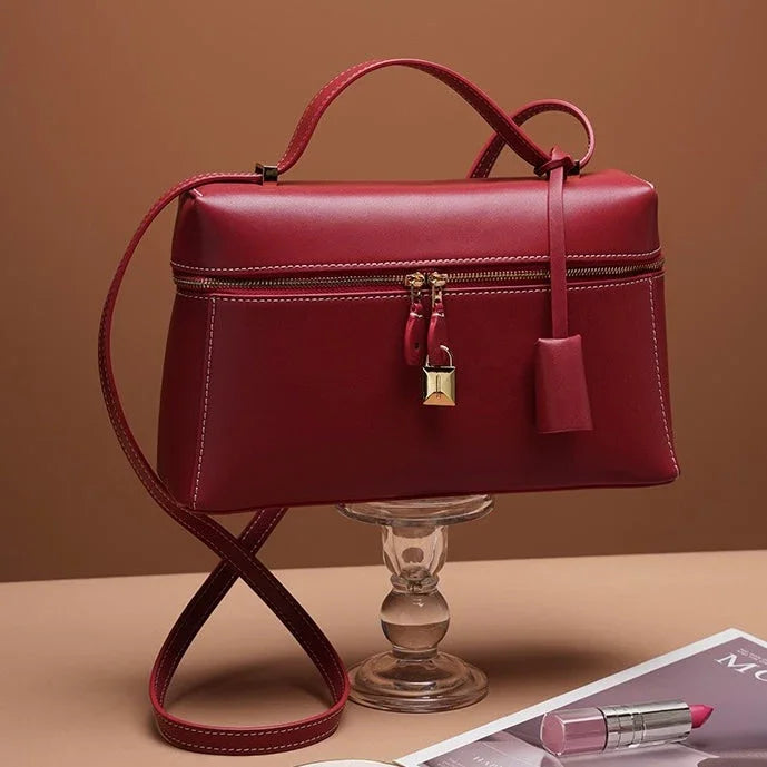 Elegant red leather handbag with gold lock on glass stand, pink lipstick nearby