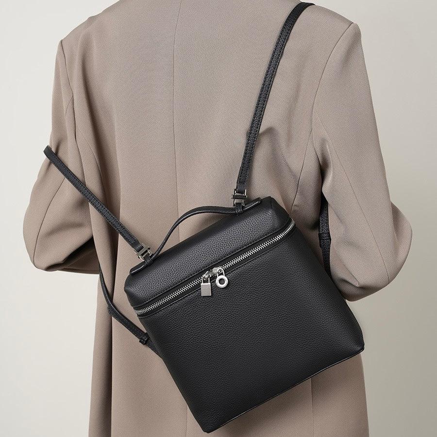 Black leather backpack with zipper on person wearing beige blazer