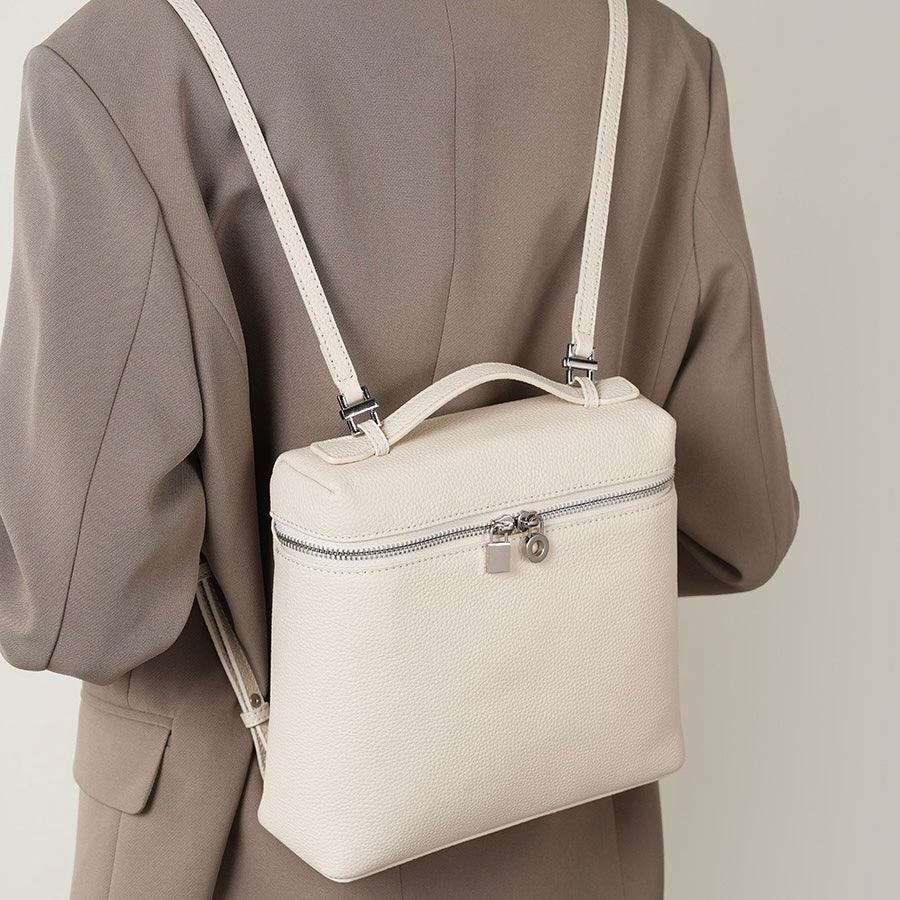Beige leather backpack with silver zippers worn over a taupe blazer