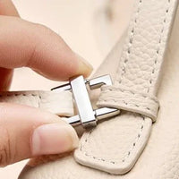 Closeup of hand fastening beige leather bag strap with silver metal buckle