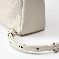 Close-up of a textured white leather handbag with an adjustable strap and silver hardware