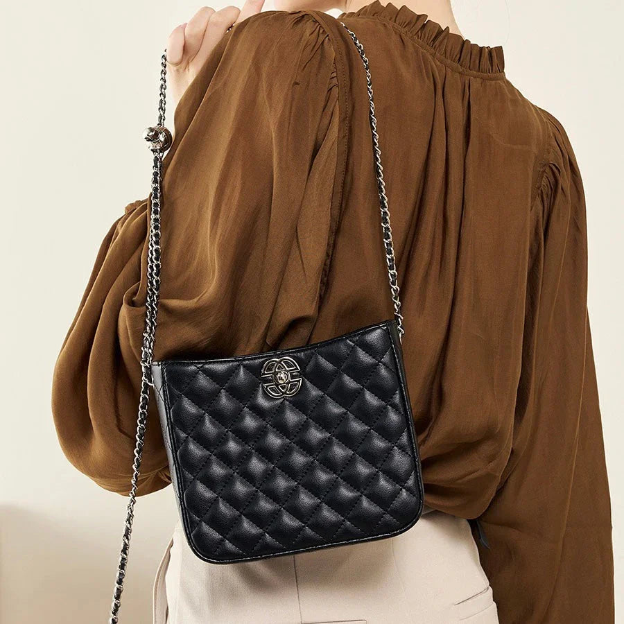 Woman wearing a brown blouse with a black quilted crossbody bag and chain strap