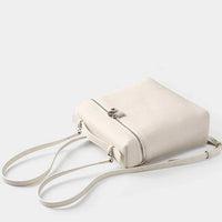 Minimalist white leather crossbody bag with zipper and adjustable strap on light background
