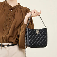 Woman holding black quilted leather shoulder bag with chain strap and gold logo, brown blouse