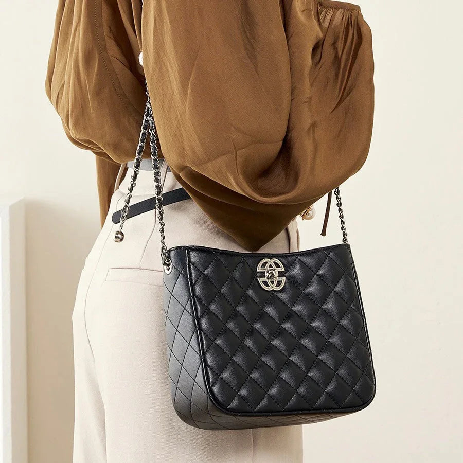 Black quilted leather shoulder bag with silver chain strap on woman in brown blouse