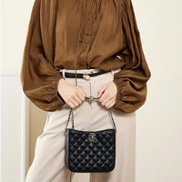 Woman wearing brown blouse and beige pants holding a black quilted leather shoulder bag