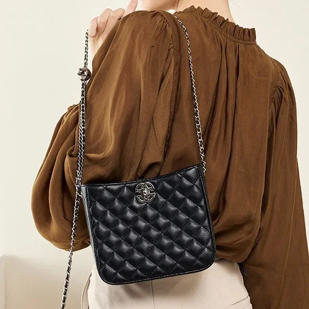 Woman wearing a brown blouse with a black quilted leather crossbody bag and chain strap