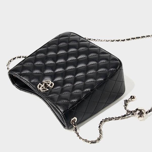 Black quilted leather crossbody bag with gold chain strap and metallic logo on white background