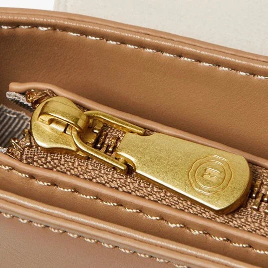 Close-up of gold zipper on tan leather bag with detailed stitching