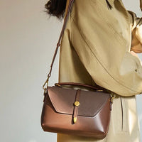 Woman in beige coat carrying a brown leather crossbody handbag with gold hardware