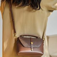 Brown leather crossbody bag with gold hardware worn over a tan coat