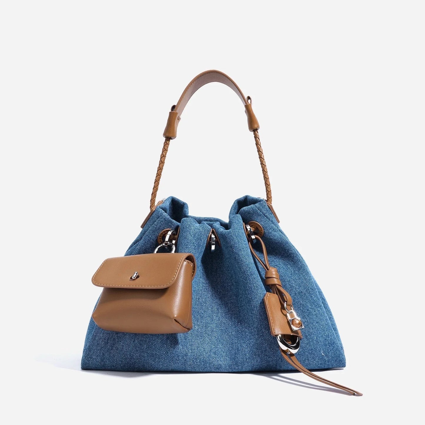 Blue denim drawstring handbag with brown leather handle and front pocket on white background.