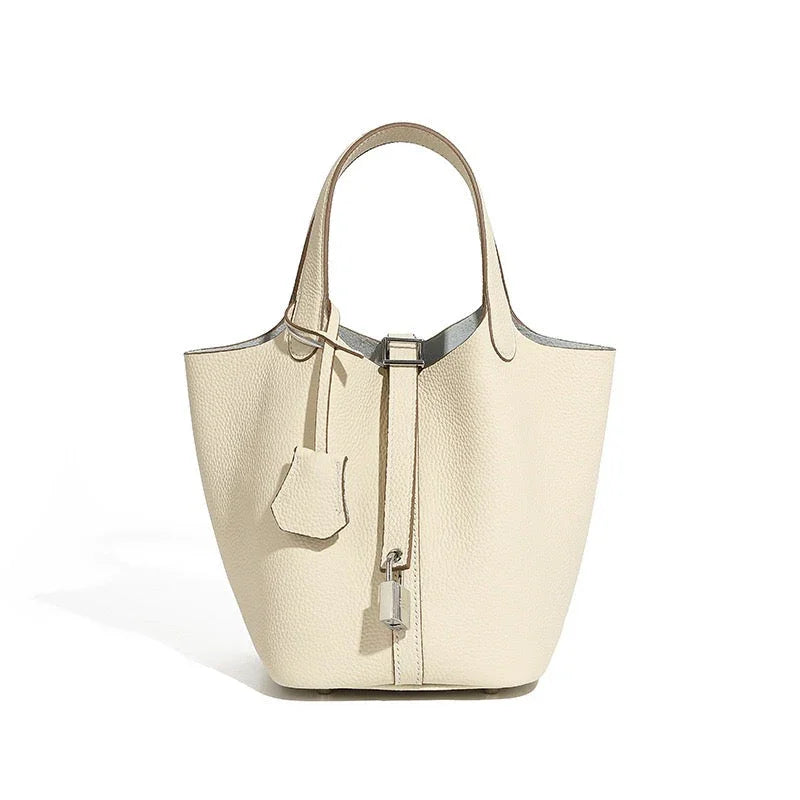 Beige leather bucket bag with top handles and silver lock accent on white background