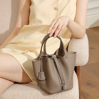 Taupe leather handbag on woman's lap in beige dress, sitting on cream chair indoors