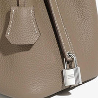 Taupe pebbled leather handbag close-up with silver lock and white stitching