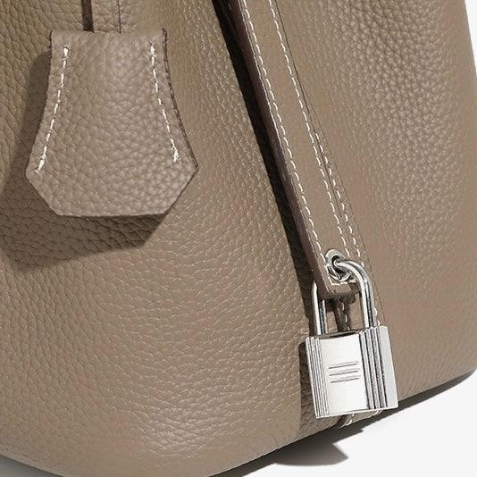 Taupe pebbled leather handbag close-up with silver lock and white stitching