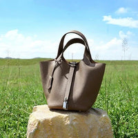 Taupe leather handbag on a stone with green grass field and blue sky background