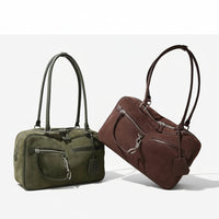 Green and brown suede handbags with silver zippers and long handles on a neutral background