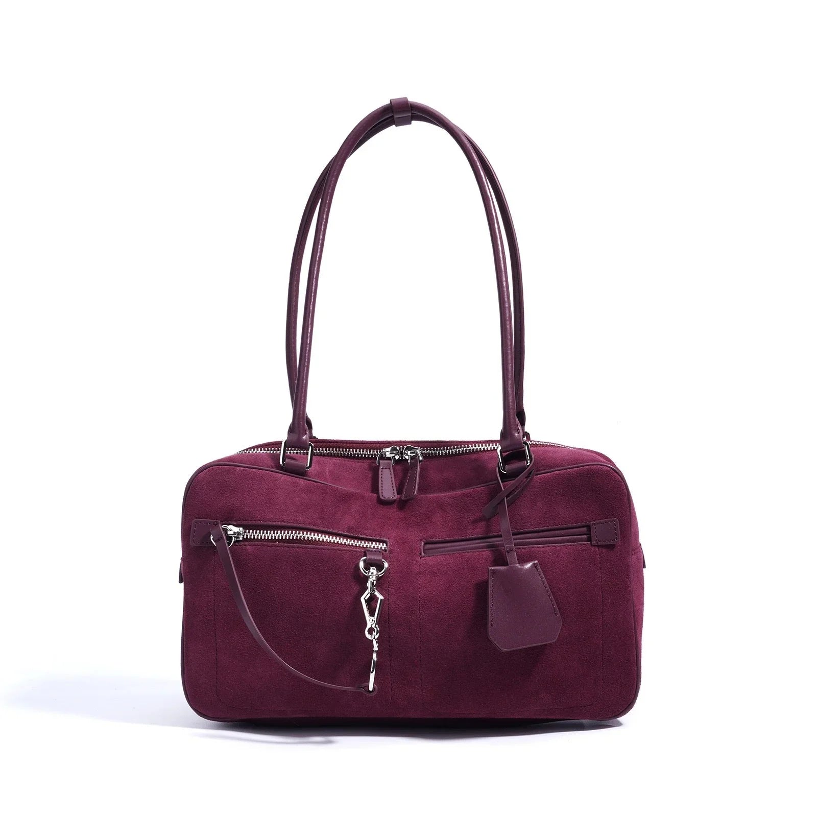 Burgundy suede handbag with double handles, front zip pockets, and silver hardware on white background