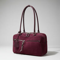 Plum suede handbag with double handles and front zip pockets on a neutral background