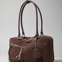 Brown suede handbag with silver zippers and long handles on a light background