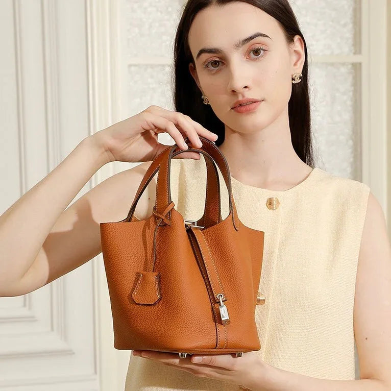Woman in beige dress holding brown leather bucket handbag with top handles indoors