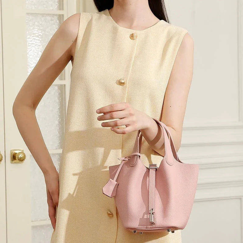 Woman in sleeveless beige dress holding a pastel pink leather tote handbag indoors