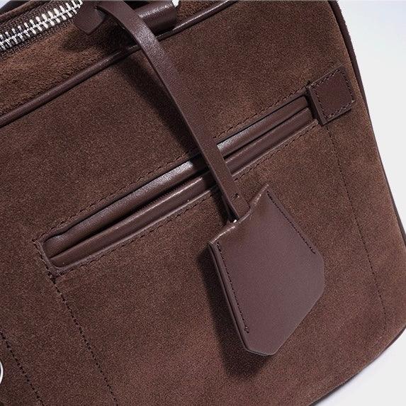 Close-up of brown suede leather handbag with zipper, pocket, and luggage tag