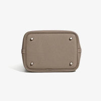 Beige pebbled leather handbag bottom with metal feet on white background