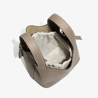Taupe leather bucket bag with drawstring closure and textured handles on white background