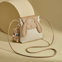 Beige crossbody bag with bunny face design and plush keychain on neutral background