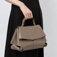 Taupe leather handbag with top handle, carried by woman in black dress