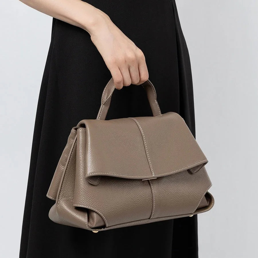Taupe leather handbag with top handle, carried by woman in black dress