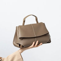 Taupe leather handbag with top handle held up against a plain white background
