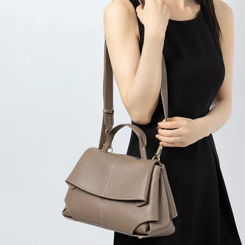Woman in black dress holding taupe leather handbag with top handle and shoulder strap
