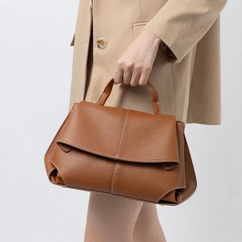 Woman in beige blazer holding a brown leather handbag, minimalist fashion accessory