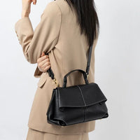 Woman in beige blazer carrying black leather handbag with shoulder strap