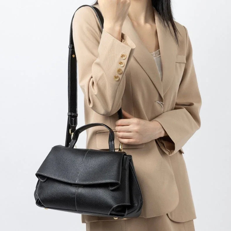 Woman in beige blazer holding black leather handbag with shoulder strap