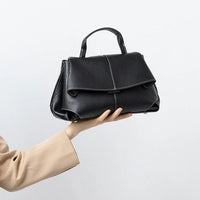 Hand holding black leather handbag with top handle against white background