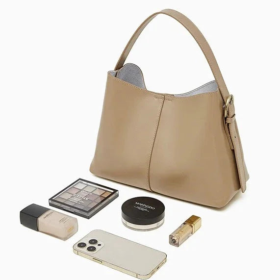 Beige leather shoulder bag with makeup, phone, and cosmetics on white background