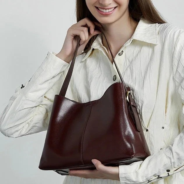 Woman holding a brown leather shoulder bag, wearing a white button-up shirt